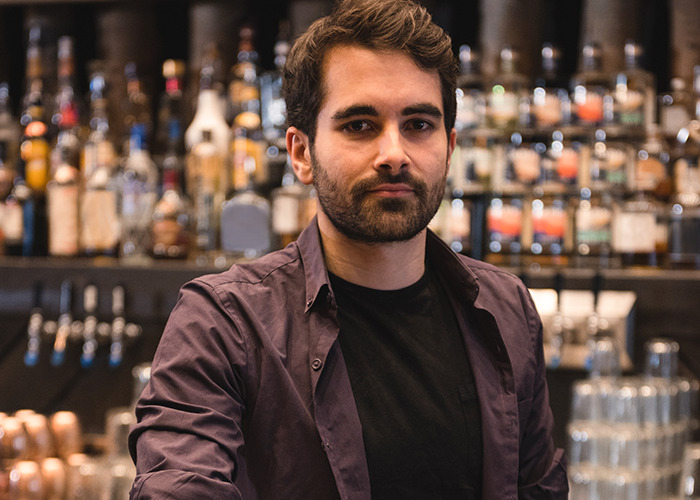 Young man standing in a bar with bottles in the background, illustrating 911 operators handling non-emergency calls.