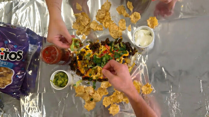 Couple preparing a shared plate of loaded nachos with chips, salsa, guacamole, and sour cream for an at-home date night.