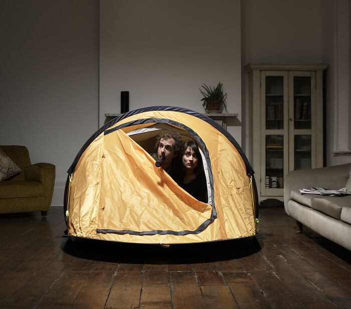 Couple enjoying an indoor camping tent setup on wooden floor as a creative at-home date night idea.
