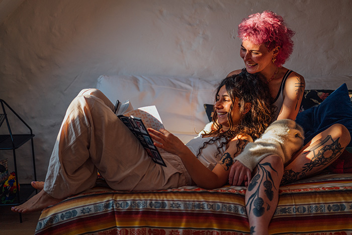 Two women relaxing on a couch enjoying at-home date night ideas with cozy lighting and reading together.