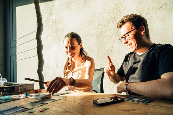 Couple enjoying at-home date night ideas playing a board game together in a sunlit room with a wooden table.