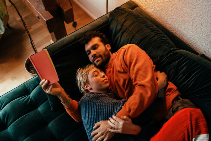 Couple cuddling on a couch, enjoying a cozy at-home date night with a book in a warm, relaxing setting.