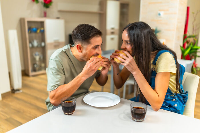 Couple enjoying at-home date night ideas by sharing burgers and drinks in a cozy dining room setting.
