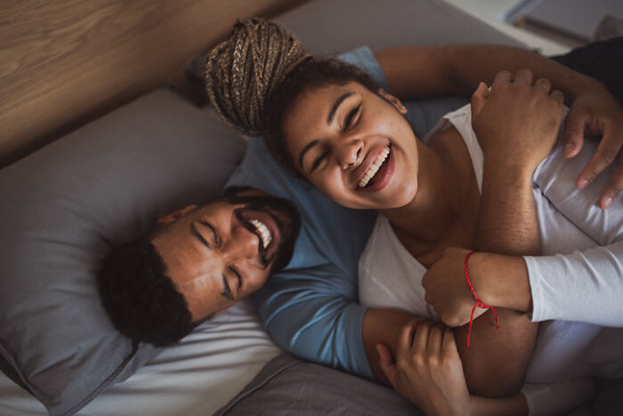 Happy couple embracing and smiling in bed, enjoying cozy and romantic at-home date night ideas together.