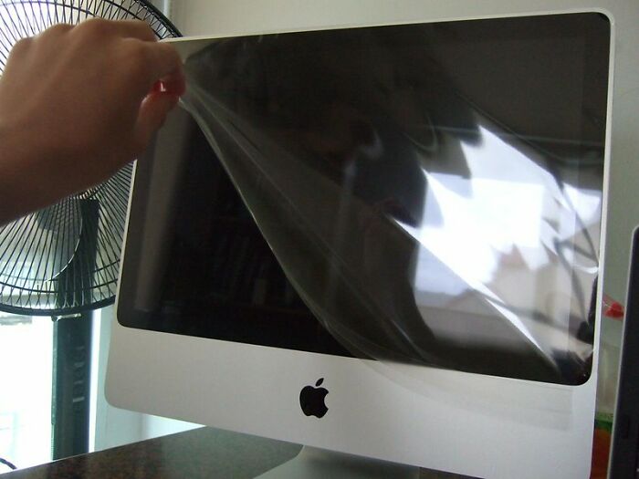 Hand peeling off protective screen from an iMac monitor showcasing a brilliantly sneaky act of revenge.