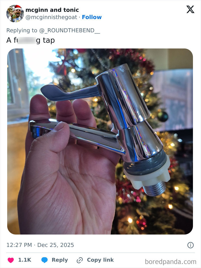 Hand holding a shiny chrome tap in front of a decorated Christmas tree, showcasing one of the worst Xmas presents received.
