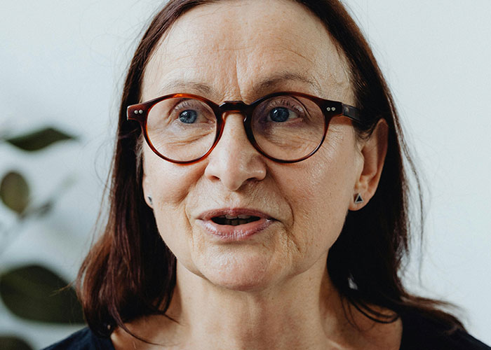 Close-up of a middle-aged woman with glasses speaking, illustrating shocked reactions to unhinged things their MIL said.