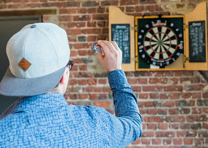 Person wearing a cap and glasses aiming a dart at a dartboard, illustrating wild stories about ex behavior.