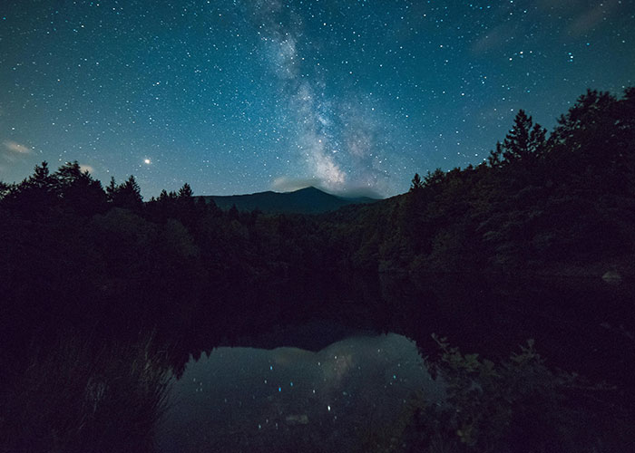 Starry night sky over a remote forest and lake, evoking creepy and mysterious things witnessed in isolated places.