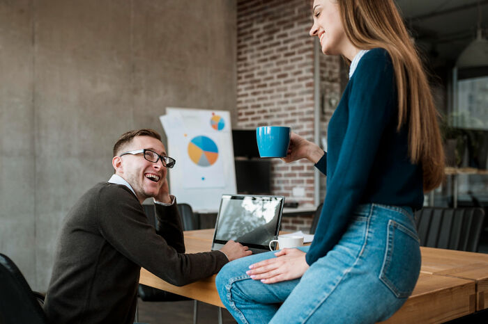 Two coworkers chatting and laughing in a modern office setting, highlighting workplace interaction and office dynamics.