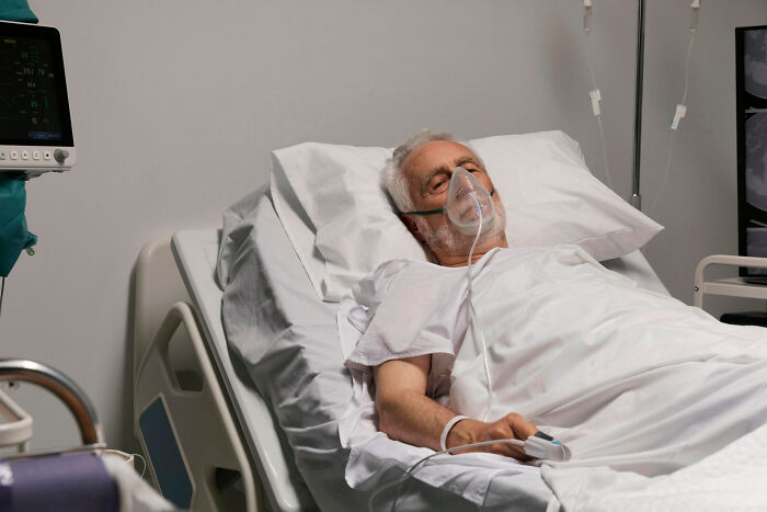 Elderly man in hospital bed with oxygen mask, capturing a moment of unintentional big family drama.