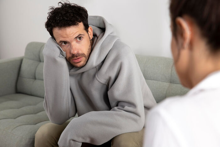 Man in a gray hoodie looking anxious while talking to someone, illustrating crazy things people do to make their ex pine for them.