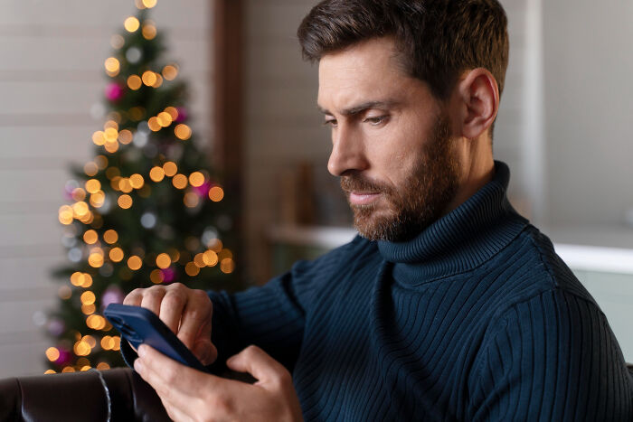 Man in navy sweater focused on phone, reflecting on crazy things people have done to make their ex pine for them.