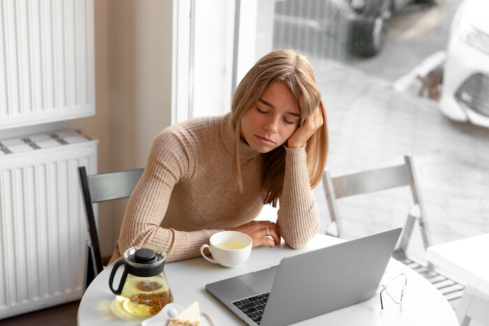 Young woman looking tired while sitting with a laptop and tea, illustrating small tricks for easier grown-up life.