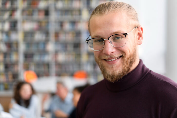 Smiling man with glasses in a casual setting, representing signs someone is still stuck in their high school era years later.