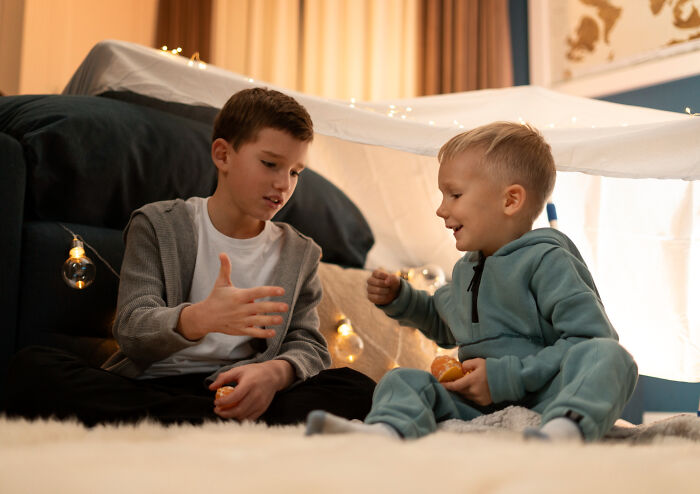 Two kids sitting inside a blanket fort sharing snacks, capturing a strange and specific kid's insult moment.
