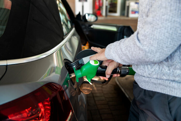 Person holding gas pump nozzle and refueling car, illustrating revenge stories with a bitter aftertaste theme.