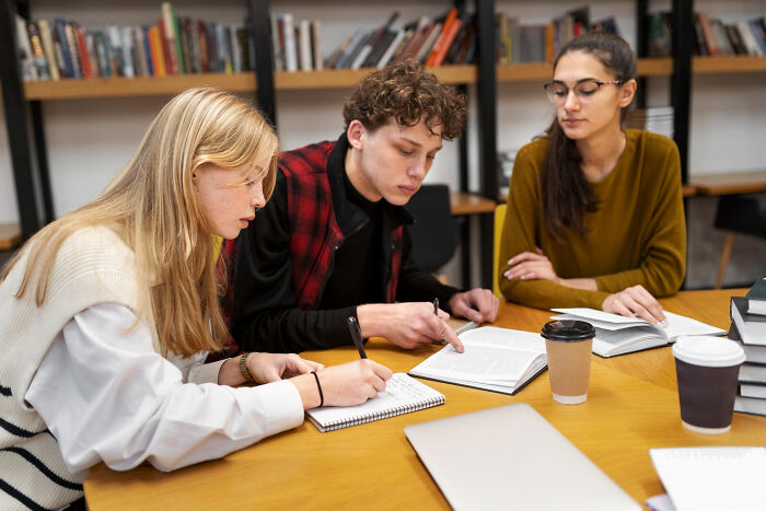 Three young adults studying together at a table with books and coffee, focused on revenge stories and lessons learned.