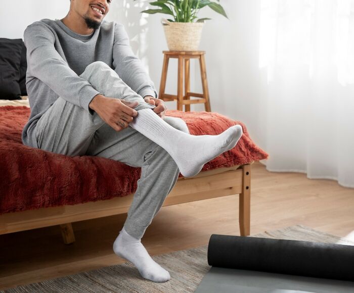 Man sitting on a bed putting on white socks, smiling, illustrating men missed delivery babies emotions and experiences.