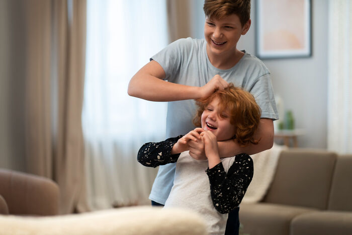 Two kids playfully wrestling indoors, captured with strange and specific kid's insults creating a unique moment.
