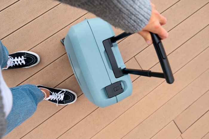 Person in casual clothes holding a blue suitcase, preparing for travel in an airport with crazy airport stories context.