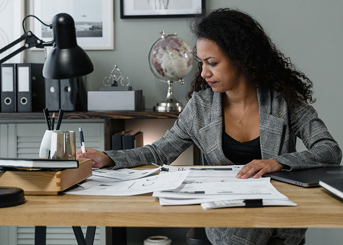 Professional woman working at desk in office, reviewing documents about luxury industries and expensive rip-offs.
