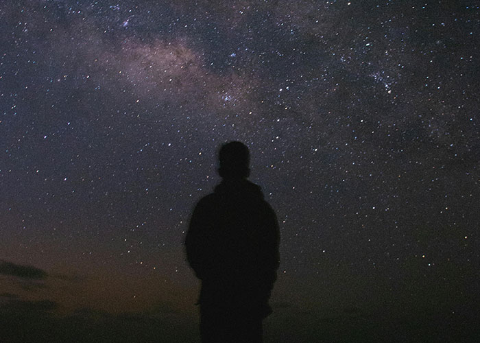 Silhouette of a person stargazing under a vast night sky, evoking creepy and mysterious scenes in remote places.