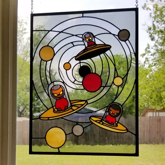 Stained glass art featuring vivid pop culture icons as colorful UFOs with alien figures in a circular space design.