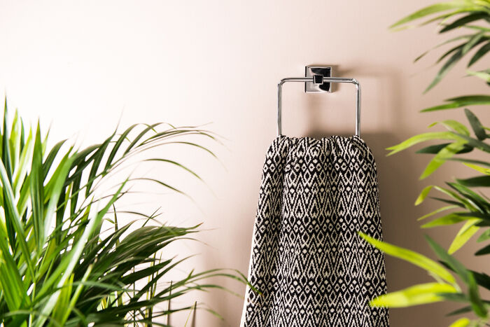 Towel with geometric pattern hanging on a metal rack surrounded by green indoor plants in a bright room.