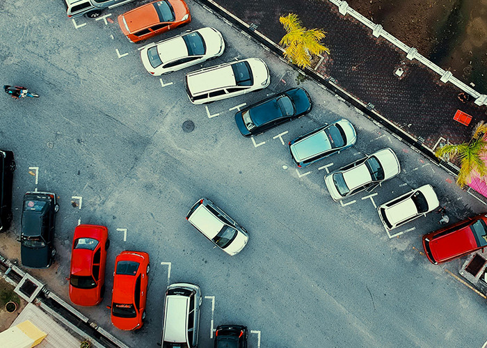 Aerial view of a parking lot with multiple cars parked and one car navigating between spaces, illustrating 911 operators' dumbest non-emergency calls.