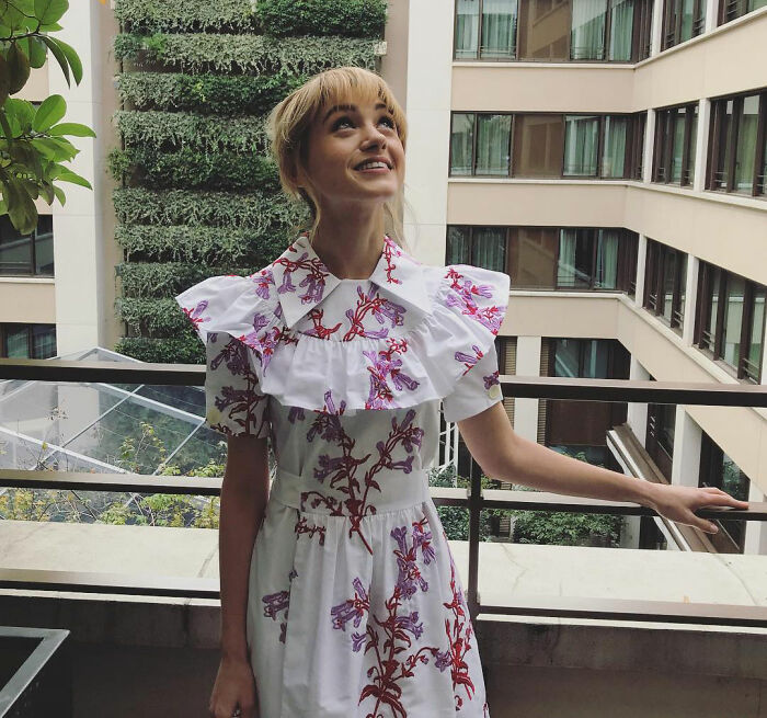 Natalia Dyer in a floral dress standing on a balcony, attracting fan attention and compared to Ariana Grande. Natalia Dyer in a floral dress standing on a balcony, attracting fan attention and compared to Ariana Grande.