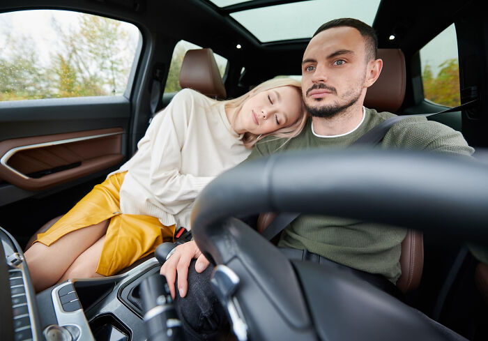 Man looking focused while driving with woman resting her head on his shoulder, depicting men missed delivery babies feeling.