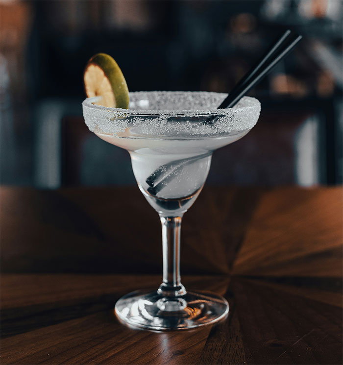 Margarita cocktail with salted rim and lime slice on wooden table, waiter serves first date disaster setting.