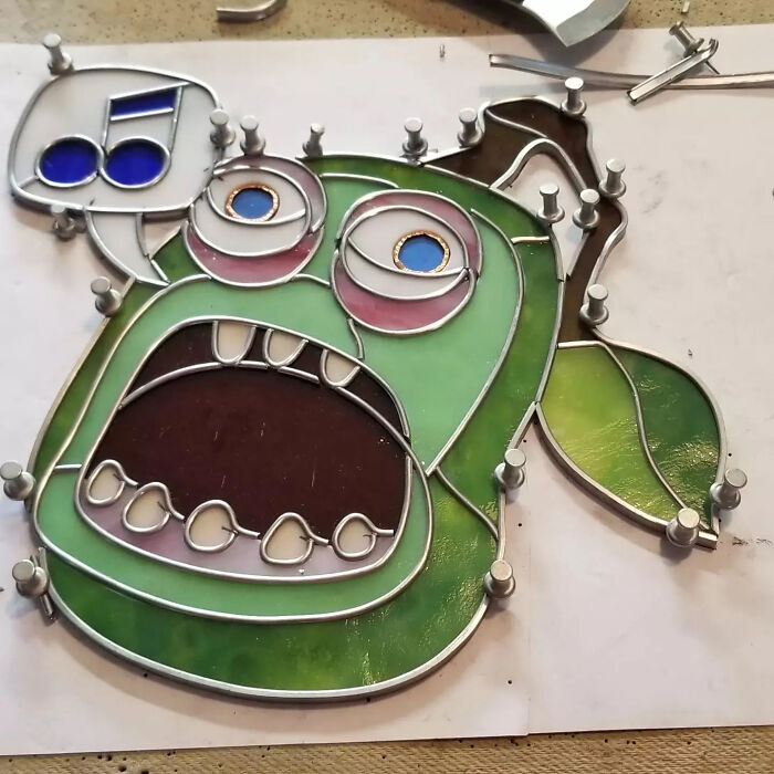 Stained glass artwork of a green pop culture icon character with wide open mouth and colorful eyes in progress.