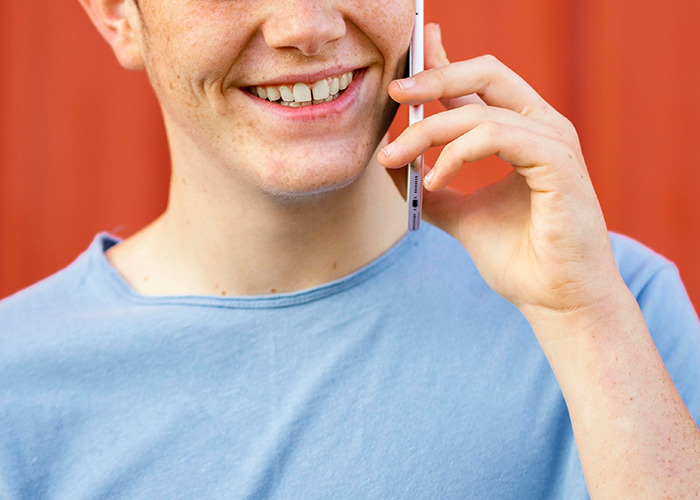 Young person smiling while talking on the phone, illustrating 911 operators handling dumb non-emergency calls.
