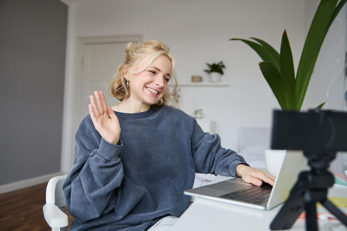 Young woman smiling and waving during a video call, capturing an embarrassing moment people were blessed to see.
