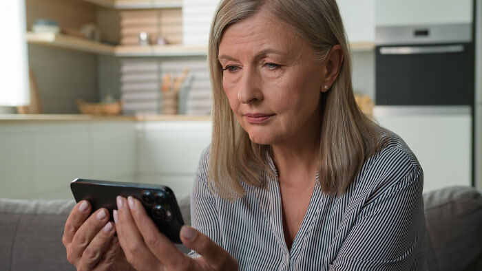 Middle-aged woman looking thoughtfully at her phone, reflecting on crazy things people have done post-breakup.