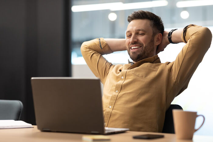 Man smiling and leaning back at desk using laptop, illustrating small tricks that make being a grown-up easier.