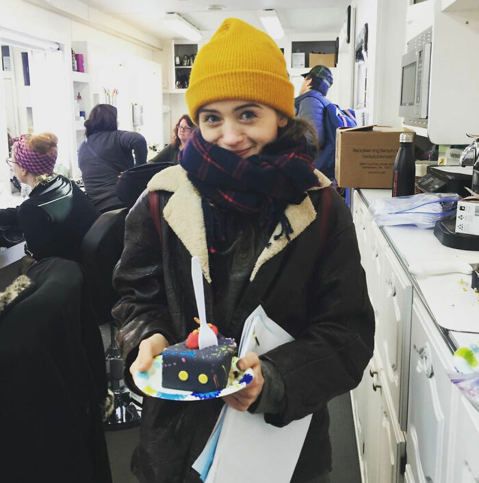 Stranger Things star Natalia Dyer wearing a yellow beanie and scarf, holding a slice of cake indoors, fans concerned with appearance. Stranger Things star Natalia Dyer wearing a yellow beanie and scarf, holding a slice of cake indoors, fans concerned with appearance.