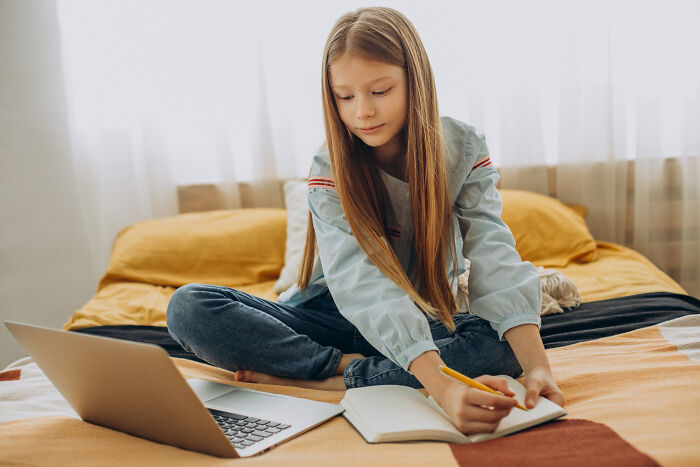 Young girl sitting on bed with laptop and notebook, using small tricks to make being a grown-up easier