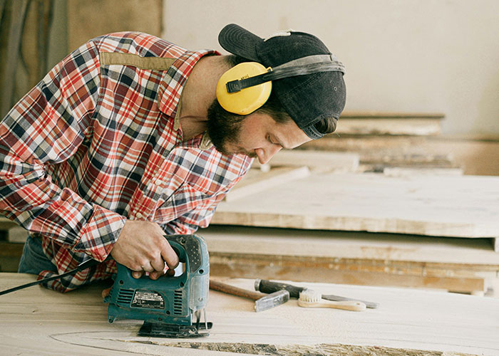 Carpenter wearing protective headphones using power tool on wood, illustrating people who work in luxury industries.