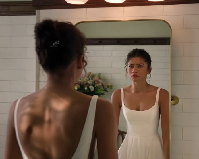 Zendaya in a white dress looking at her reflection in a bathroom mirror, related to Robert Pattinson and Zendaya engagement. Zendaya in a white dress looking at her reflection in a bathroom mirror, related to Robert Pattinson and Zendaya engagement.