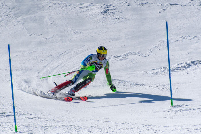 Skier in competitive gear racing down snowy slope between gates, illustrating dedication beyond once famous regular job.