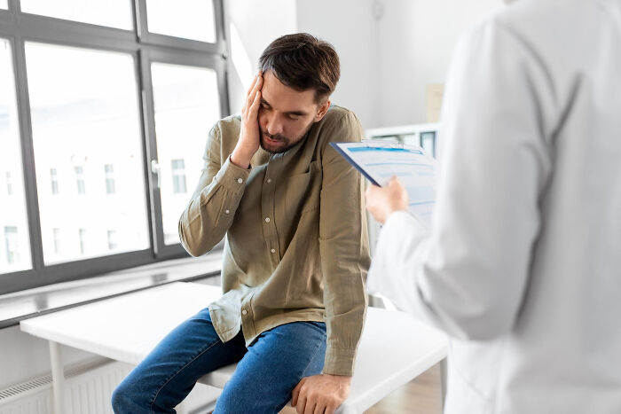 Man looking stressed while sitting on a medical exam table, missing delivery of babies concerns in a clinic setting.