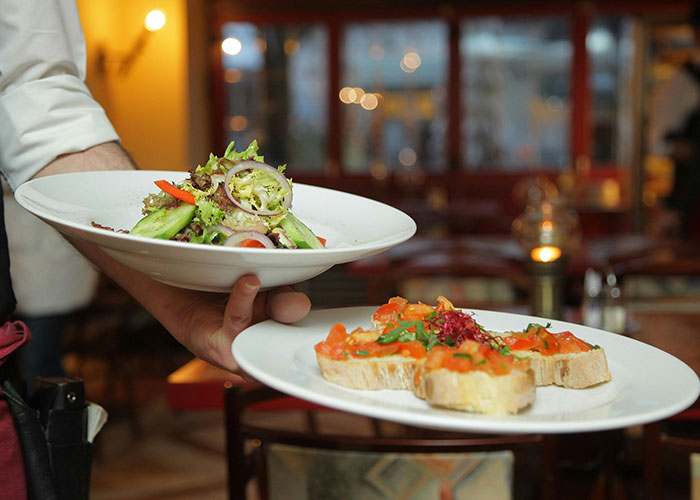 Waiter serving luxury food dishes in an upscale restaurant, illustrating items the rich pay for that are rip-offs.