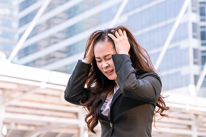 Frustrated woman in office attire holding her head, reacting to Christmas music blasting loudly at work.