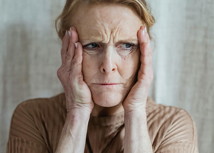 Older woman with a distressed expression holding her face, representing a toxic mother-in-law upset at a casual Christmas gathering.