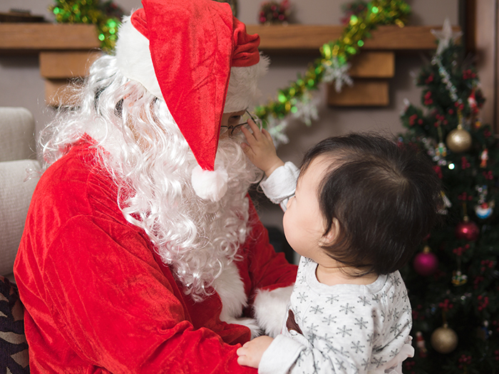 Baby reaching out to Santa Claus sitting by Christmas tree during festive holiday celebration indoors. Baby reaching out to Santa Claus sitting by Christmas tree during festive holiday celebration indoors.