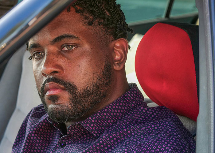 Man with a serious expression sitting in a car, reflecting on wild stories people shared about their exes.