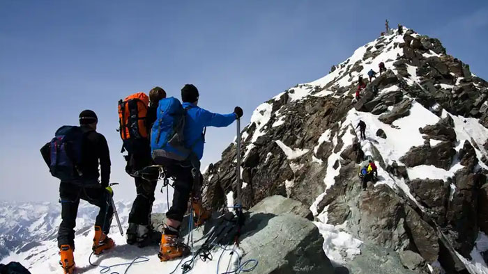 Three climbers in winter gear ascending Austria’s highest peak with snow and rocky terrain under clear blue sky. Three climbers in winter gear ascending Austria’s highest peak with snow and rocky terrain under clear blue sky.